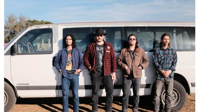 A group of musicians stands in front of a touring van